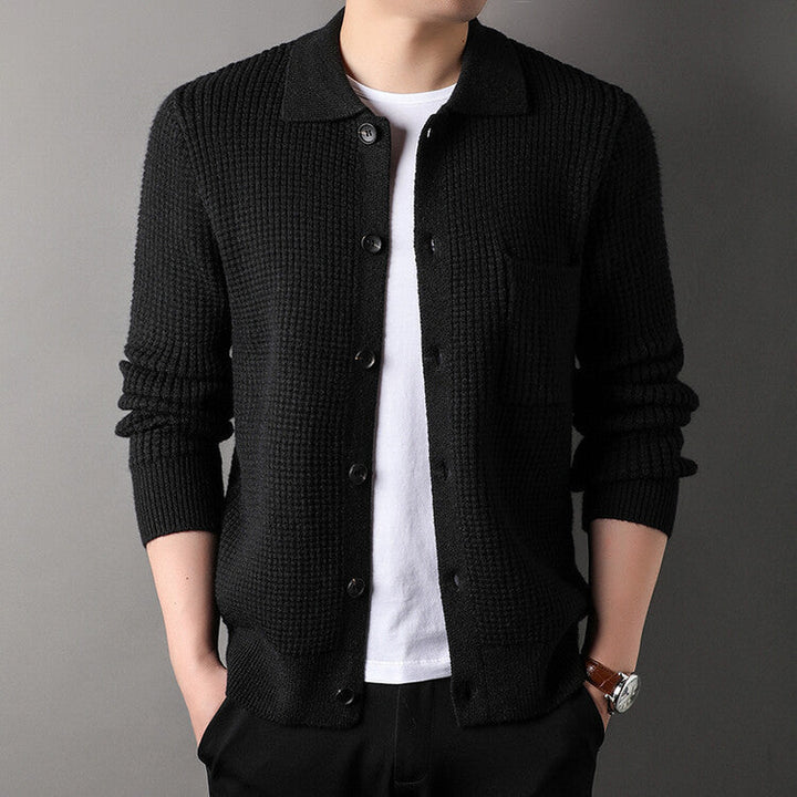 Uomo con cardigan nero a maglia grossa, camicia bianca sotto, mani in tasca. Moda maschile elegante, abbigliamento casual autunnale.