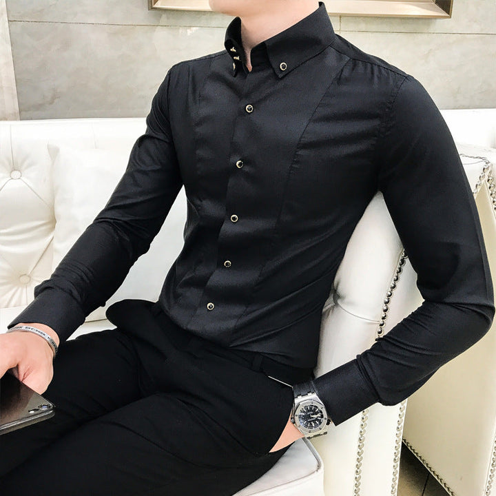 Uomo seduto su divano bianco indossa camicia nera elegante con bottoni, pantaloni abbinati e orologio da polso. Moda maschile, abbigliamento formale.