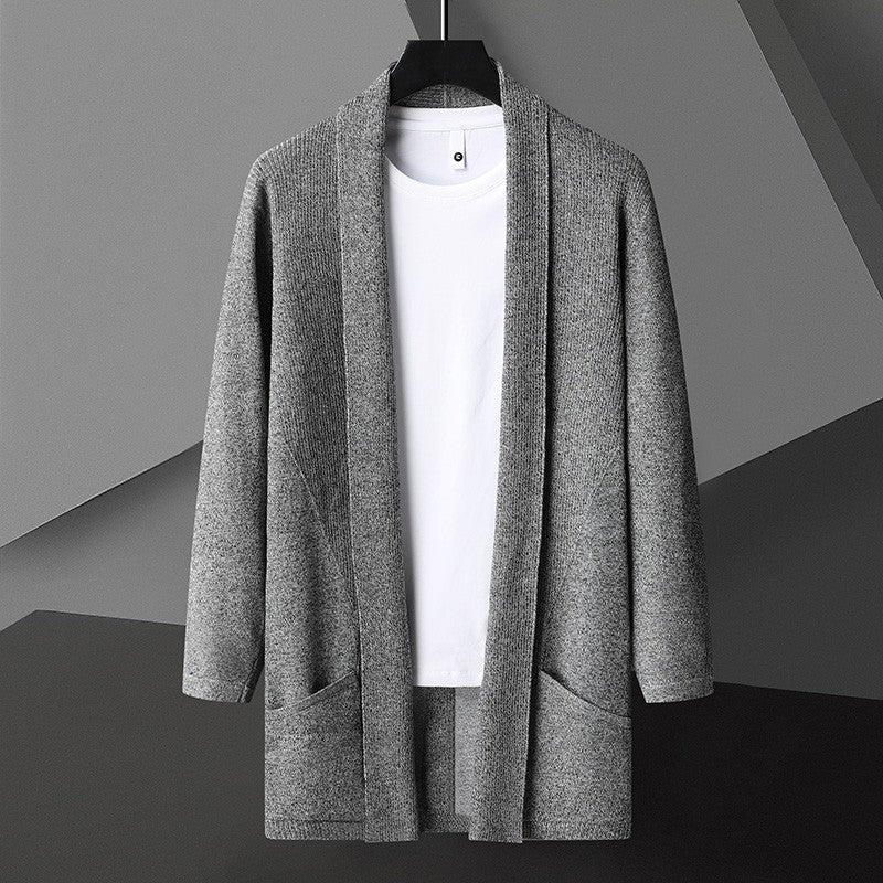 Cardigan grigio in maglia su sfondo geometrico, appeso su gruccia, con maglietta bianca sotto. Moda uomo, abbigliamento casual elegante.