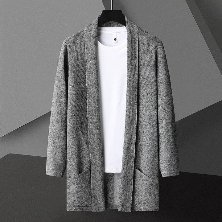 Cardigan grigio in maglia su sfondo geometrico, appeso su gruccia, con maglietta bianca sotto. Moda uomo, abbigliamento casual elegante.