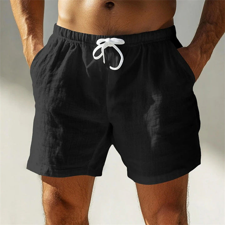 Uomo in pantaloncini neri da spiaggia con tasche, cordoncino bianco, tessuto leggero. Abbigliamento estivo maschile, moda casual.