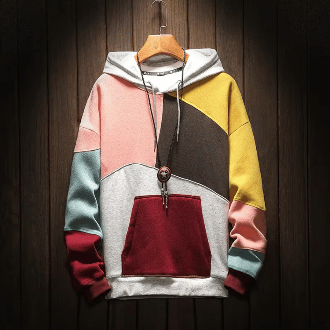 Felpa con cappuccio multicolore a blocchi, design geometrico, tasca frontale, appesa su sfondo in legno scuro. Moda casual, abbigliamento autunnale.