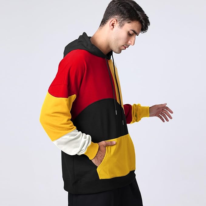 Giovane uomo con felpa multicolore a blocchi rosso, nero, giallo e bianco, cappuccio e tasca frontale. Moda casual uomo, abbigliamento streetwear.