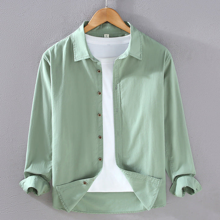Camicia verde chiaro da uomo su gruccia, maniche lunghe arrotolate, abbinata a t-shirt bianca. Moda casual, abbigliamento maschile elegante.
