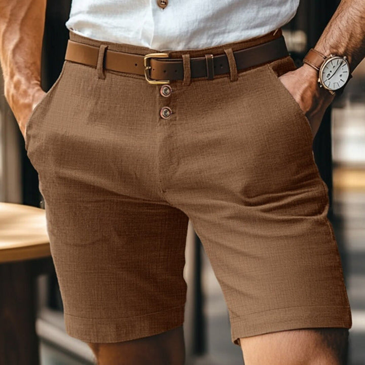 Uomo in pantaloncini marroni eleganti, camicia bianca, cintura in pelle e orologio da polso. Moda estiva maschile, abbigliamento casual chic.