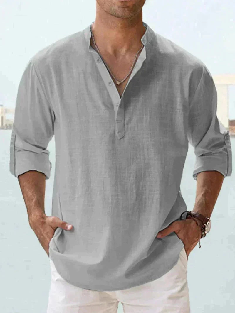 Camicia uomo lino grigia con colletto alla coreana, maniche lunghe arrotolate, abbinata a pantaloni bianchi. Stile casual elegante estivo.