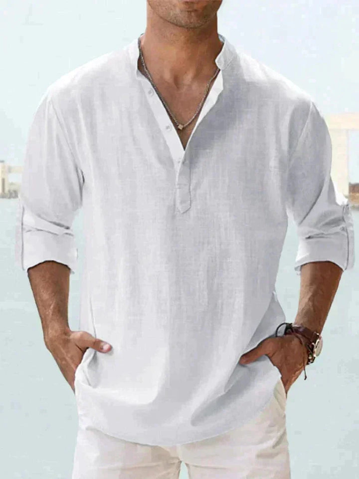 Camicia uomo bianca in lino, maniche lunghe arrotolate, collo alla coreana, stile casual estivo. Sfondo sfocato, look elegante e rilassato.