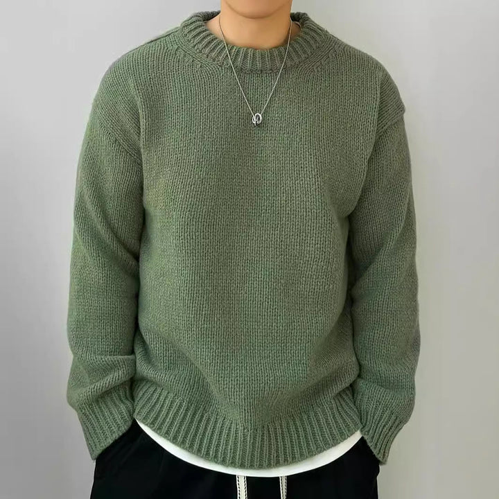 Maglione verde oliva in lana, indossato con collana argento, su sfondo grigio. Moda autunnale, abbigliamento casual, stile confortevole.