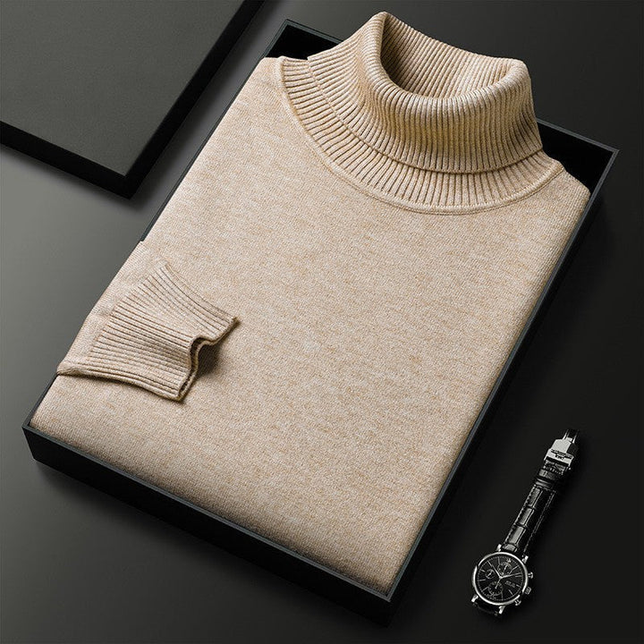 Maglione dolcevita beige piegato in scatola nera su sfondo scuro, accanto a orologio da polso elegante. Moda uomo, abbigliamento invernale.