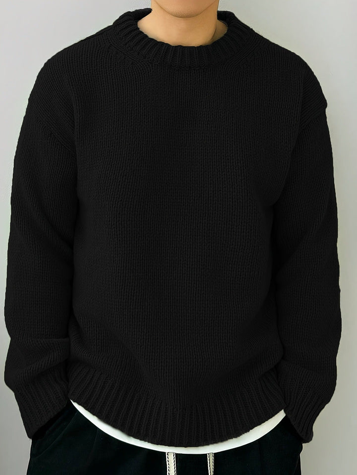 Maglione nero in lana, design a maglia grossa, indossato sopra una maglietta bianca. Moda invernale, abbigliamento casual, stile minimalista.
