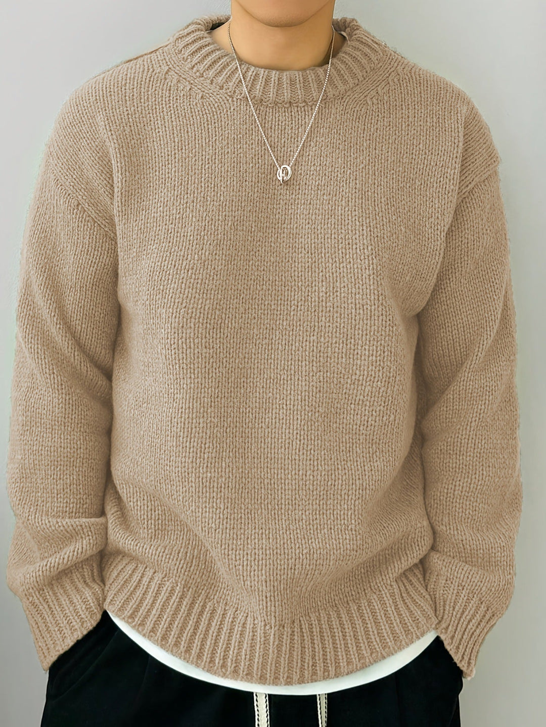 Maglione beige in lana lavorata a maglia, indossato con collana d'argento e pantaloni neri. Moda autunnale, abbigliamento casual elegante.