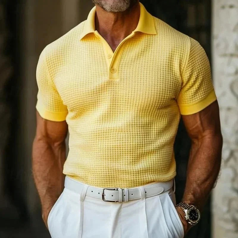 Uomo in polo gialla a trama waffle, pantaloni bianchi eleganti, cintura bianca, orologio da polso. Moda estiva maschile, stile casual chic.