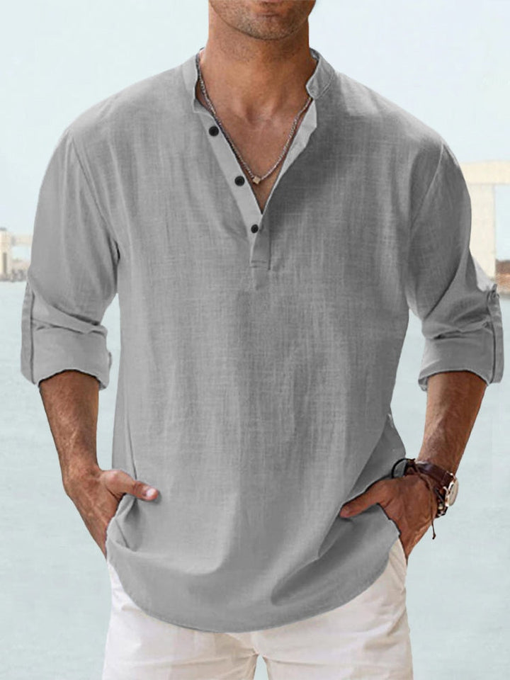 Camicia uomo lino grigia, maniche lunghe arrotolate, colletto alla coreana, abbottonatura parziale, stile casual estivo, sfondo marino.