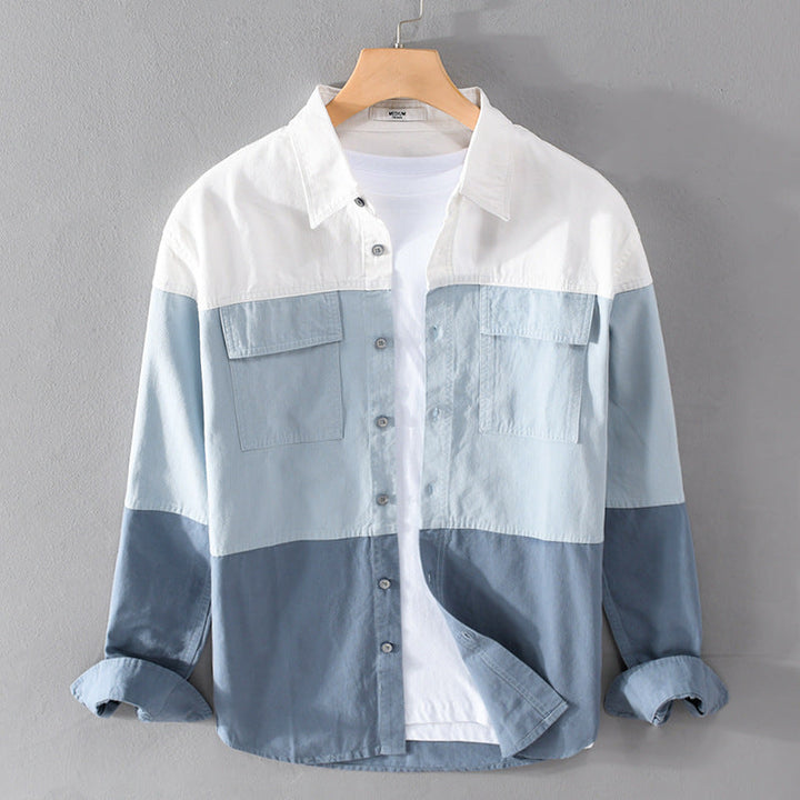 Camicia a maniche lunghe da uomo in cotone, design a blocchi di colore blu e bianco, con tasche frontali, appesa su gruccia di legno.