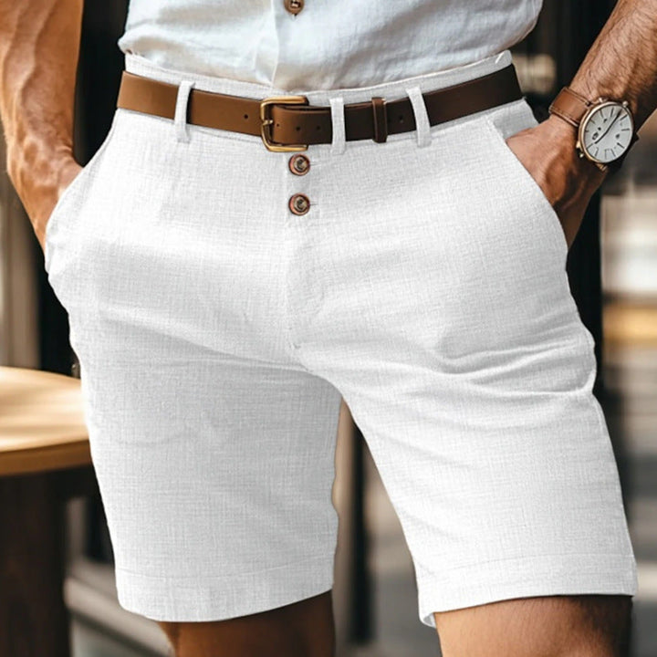Uomo in pantaloncini bianchi di lino, cintura marrone, camicia bianca, orologio da polso. Moda estiva maschile elegante e casual.