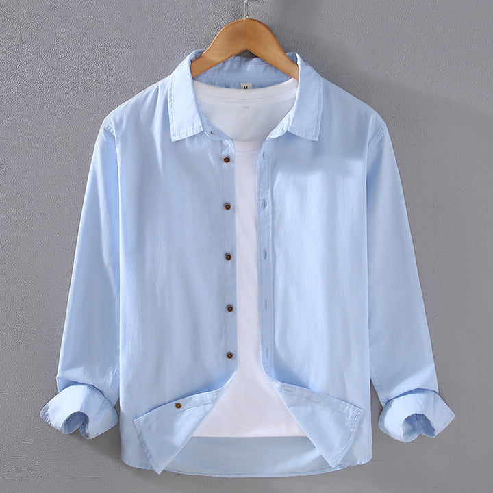 Camicia azzurra da uomo su gruccia, con bottoni marroni e maniche arrotolate, sopra una maglietta bianca. Moda casual, abbigliamento maschile elegante.