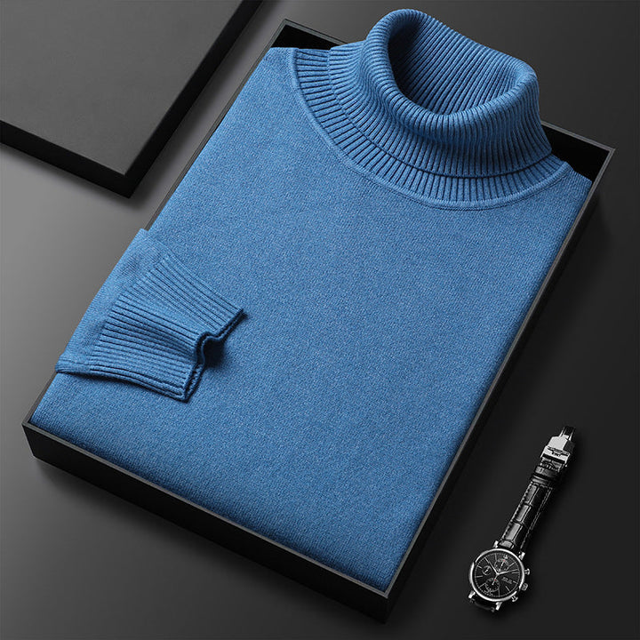 Maglione dolcevita blu piegato in scatola nera su sfondo scuro, accanto a orologio da polso elegante. Moda uomo, abbigliamento invernale di lusso.